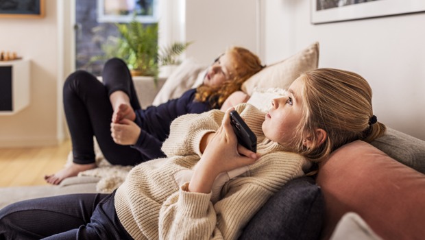 Två flickor ligger och lyssnar på en talbok i en mobiltelefon.