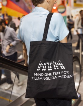  En kvinna åker rulltrappa på Bokmässan. Hon har en MTM-tygkasse på sig.