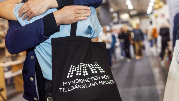  Två personer omfamnar varandra på Bokmässan, en av dem har en MTM-tygkasse på ryggen.