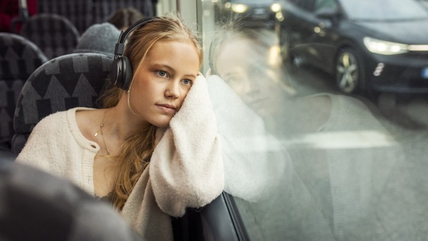 En ung tjej sitter och lyssnar på en ljudbok på  bussen.