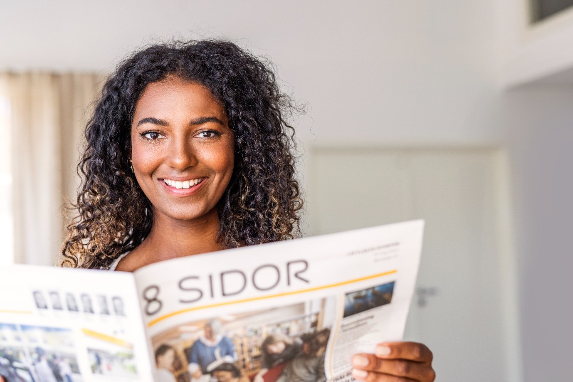 En läsare håller upp tidningen 8 Sidor. Hon ler och tittar in i kameran.