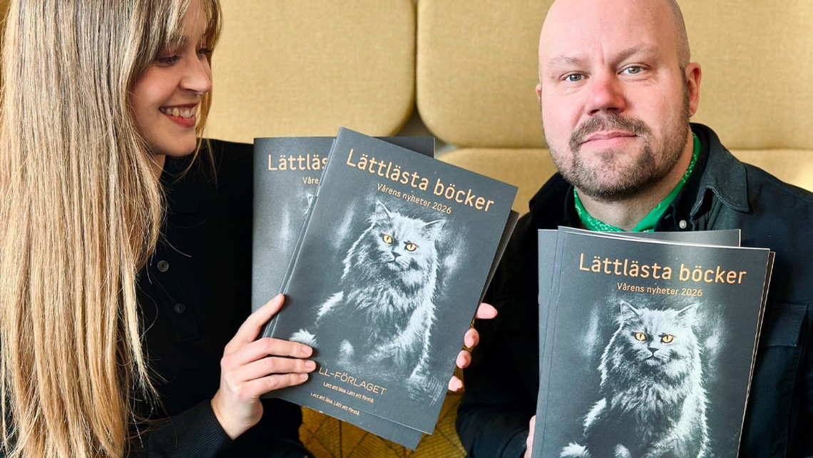 Två personer håller upp LL-förlagets nya katalog, på omslaget en svart katt.