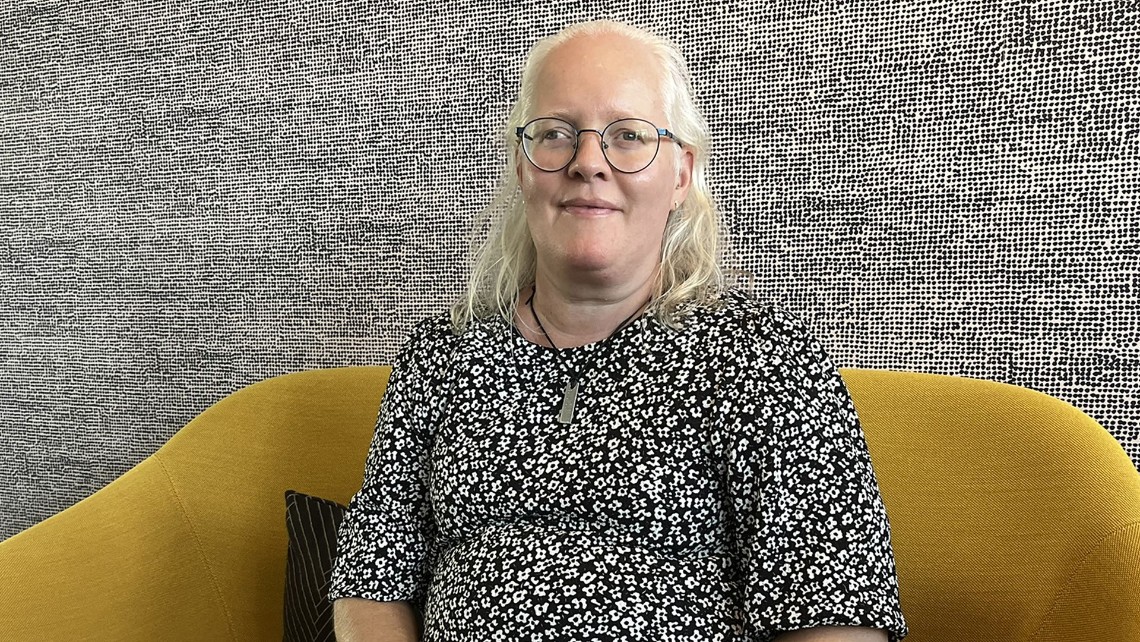 Porträttbild av Linda Eriksson som sitter i en gul soffa. Linda har glasögon och en svartvit blus. Bilden är länkad till en intervju med henne.